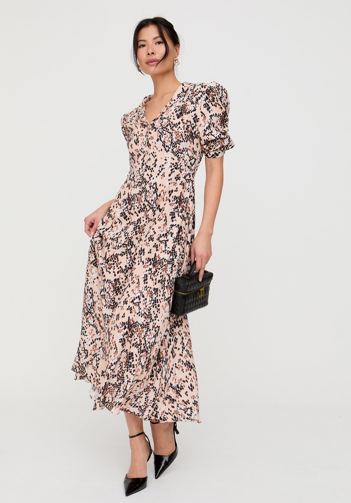 Woman wearing a floral dress holding a clutch against a white background