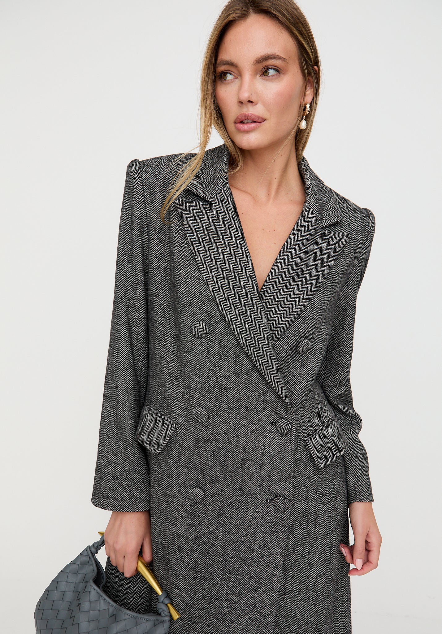 Woman wearing a gray coat holding a matching handbag against a white background