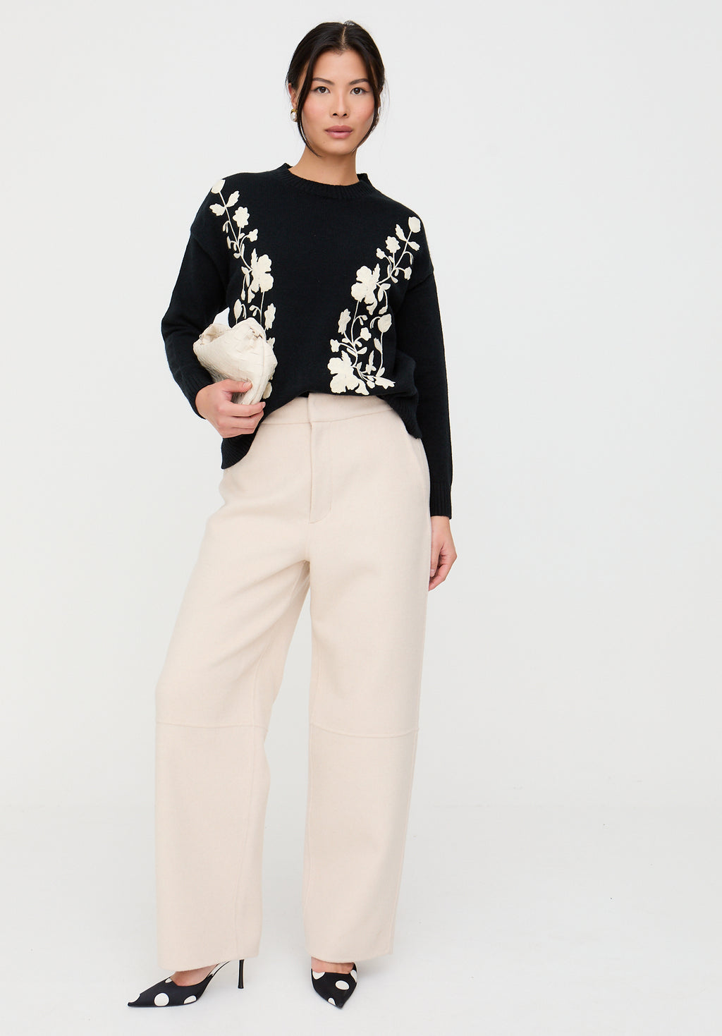 Woman wearing a black sweater with white floral patterns and beige pants on a white background