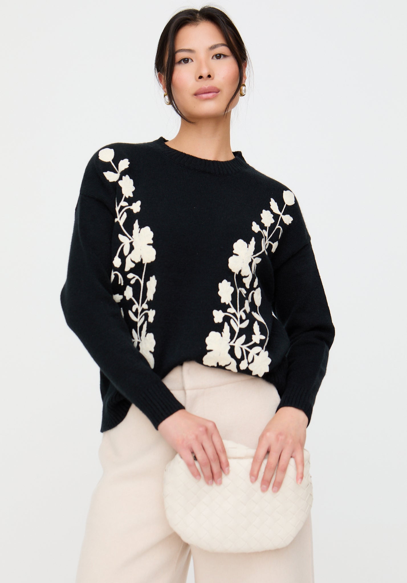 Woman wearing a black sweater with white floral patterns on a plain background