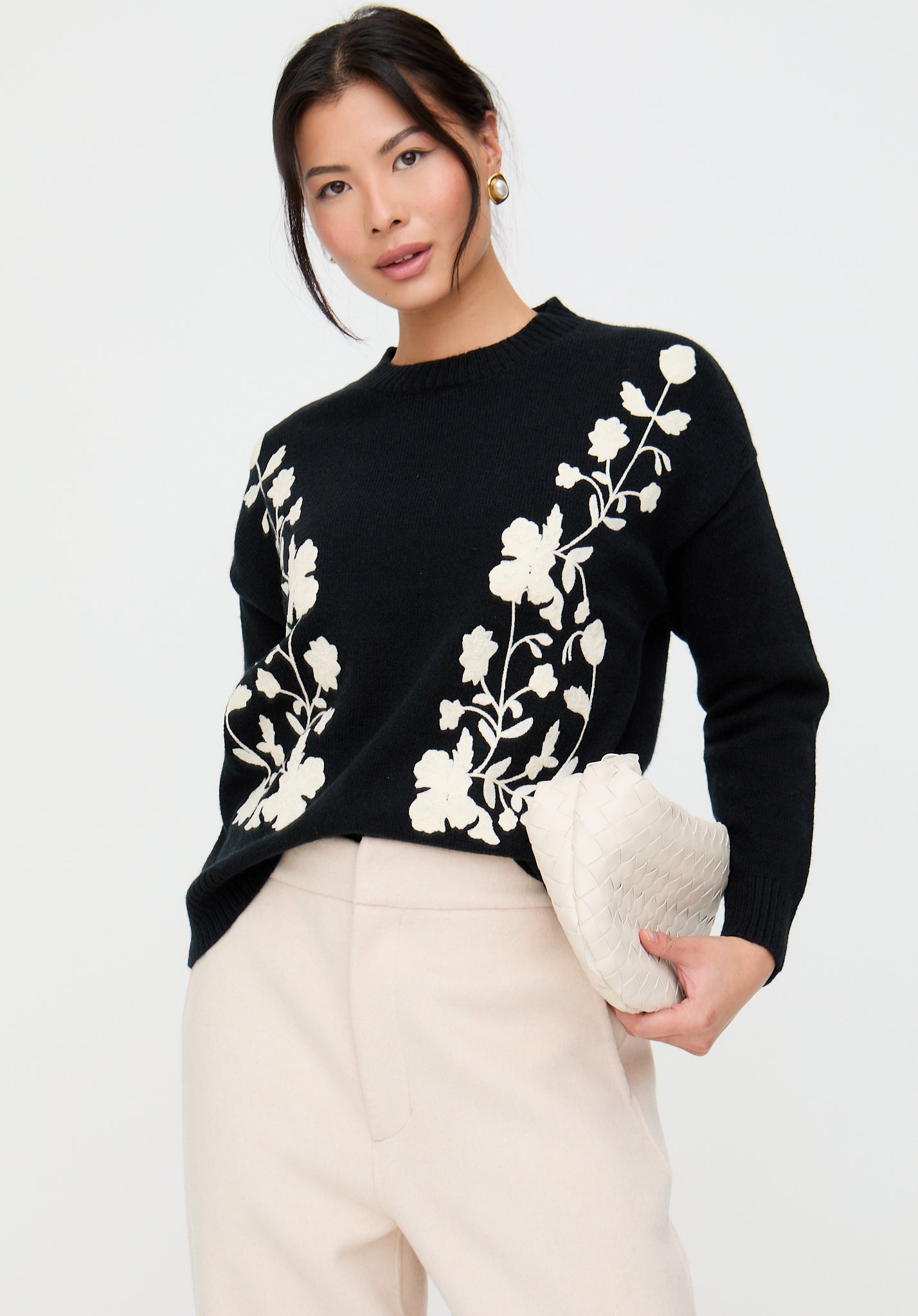 Woman wearing a black sweater with white floral patterns on a white background