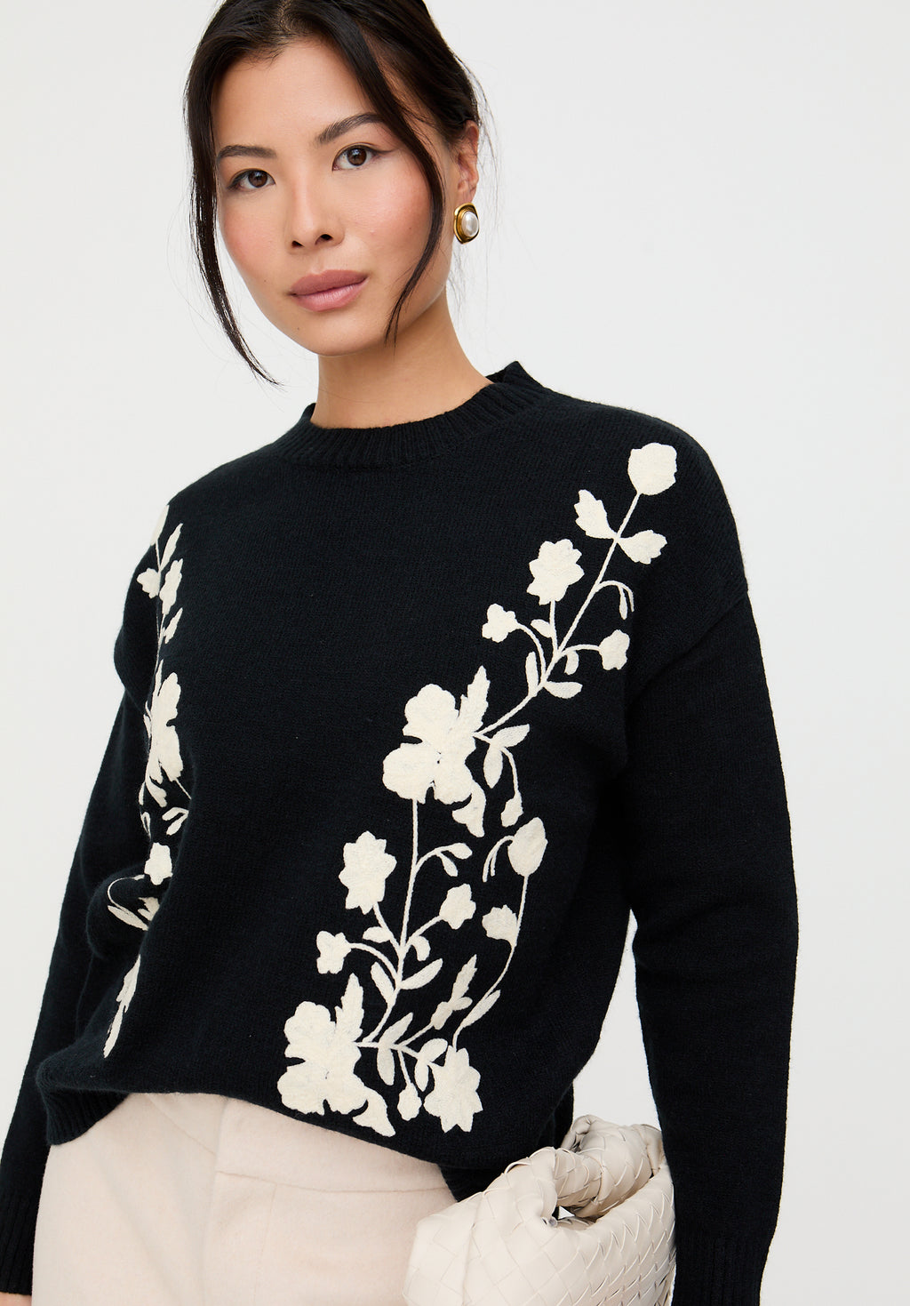 Woman wearing a black sweater with white floral embroidery on a white background