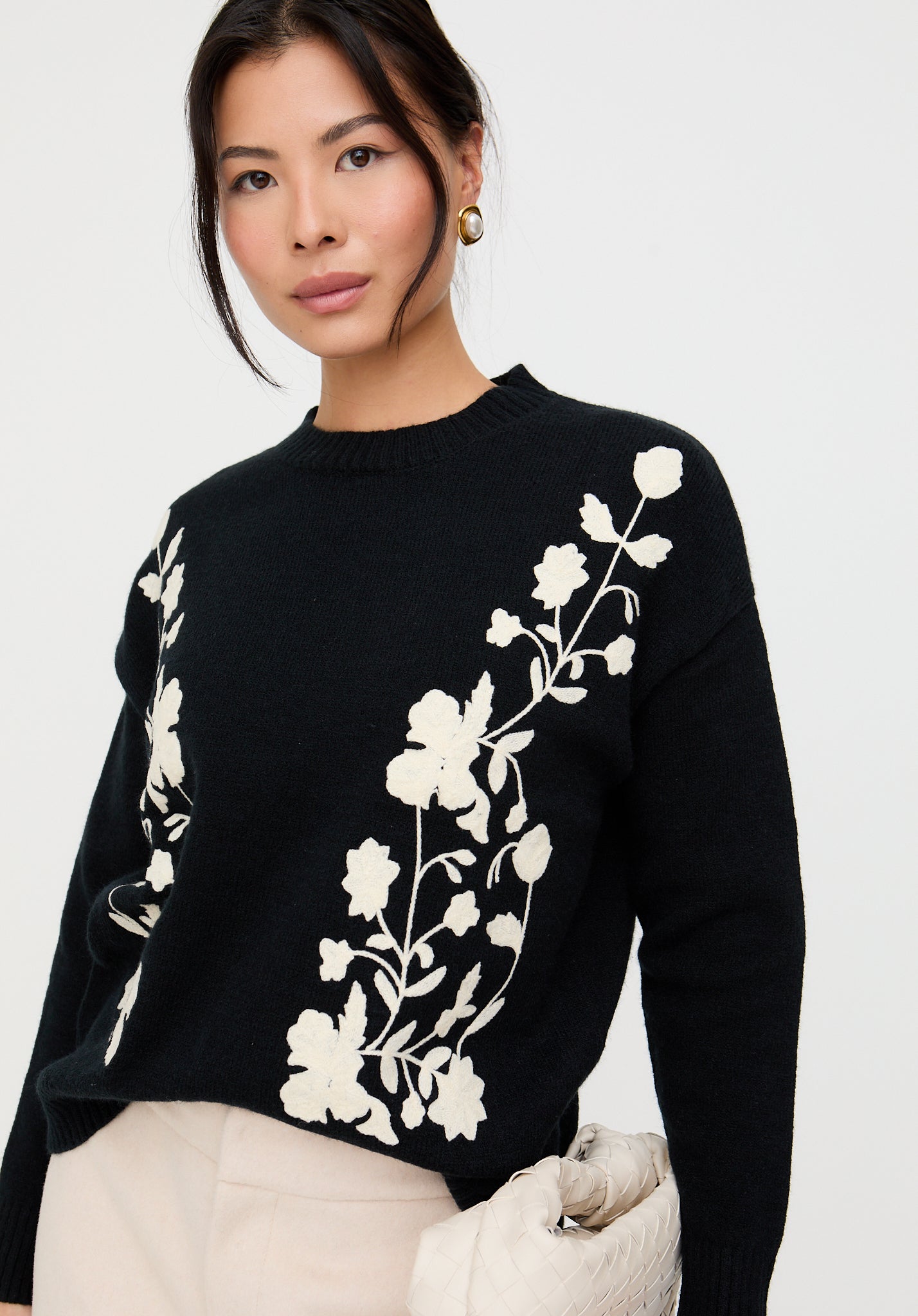 Woman wearing a black sweater with white floral embroidery on a white background