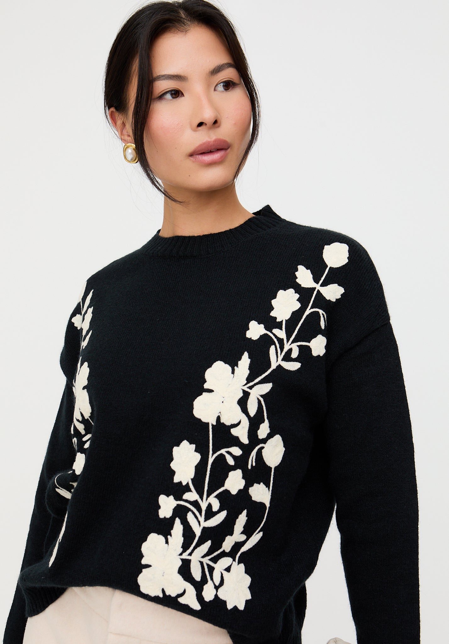 Woman wearing a black sweater with white floral embroidery against a plain background