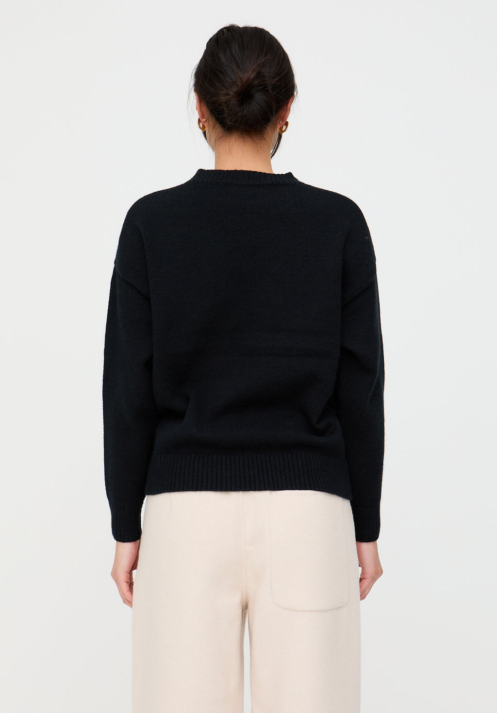 Person wearing a black sweater and white pants on a light gray background