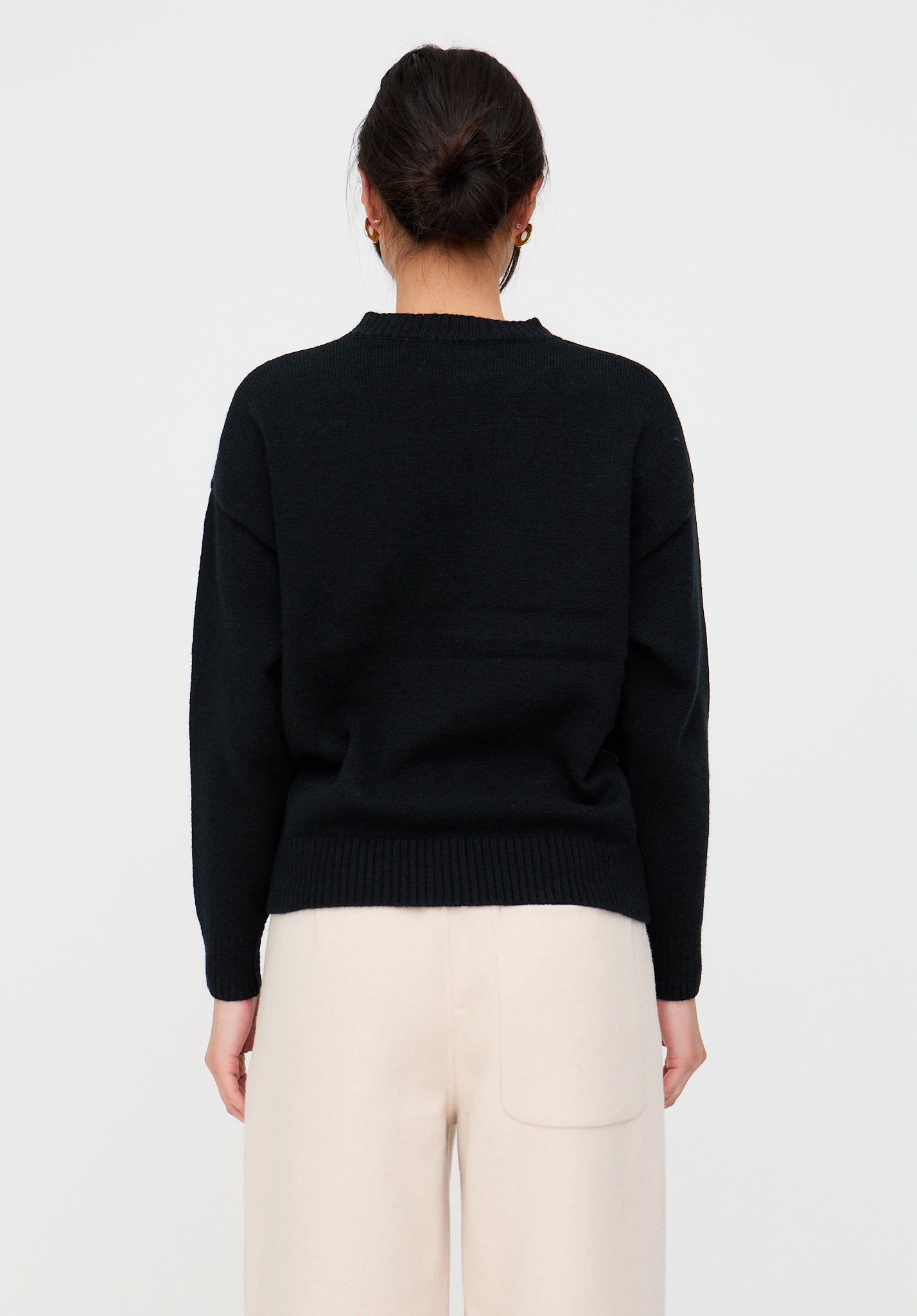 Person wearing a black sweater and white pants on a light gray background