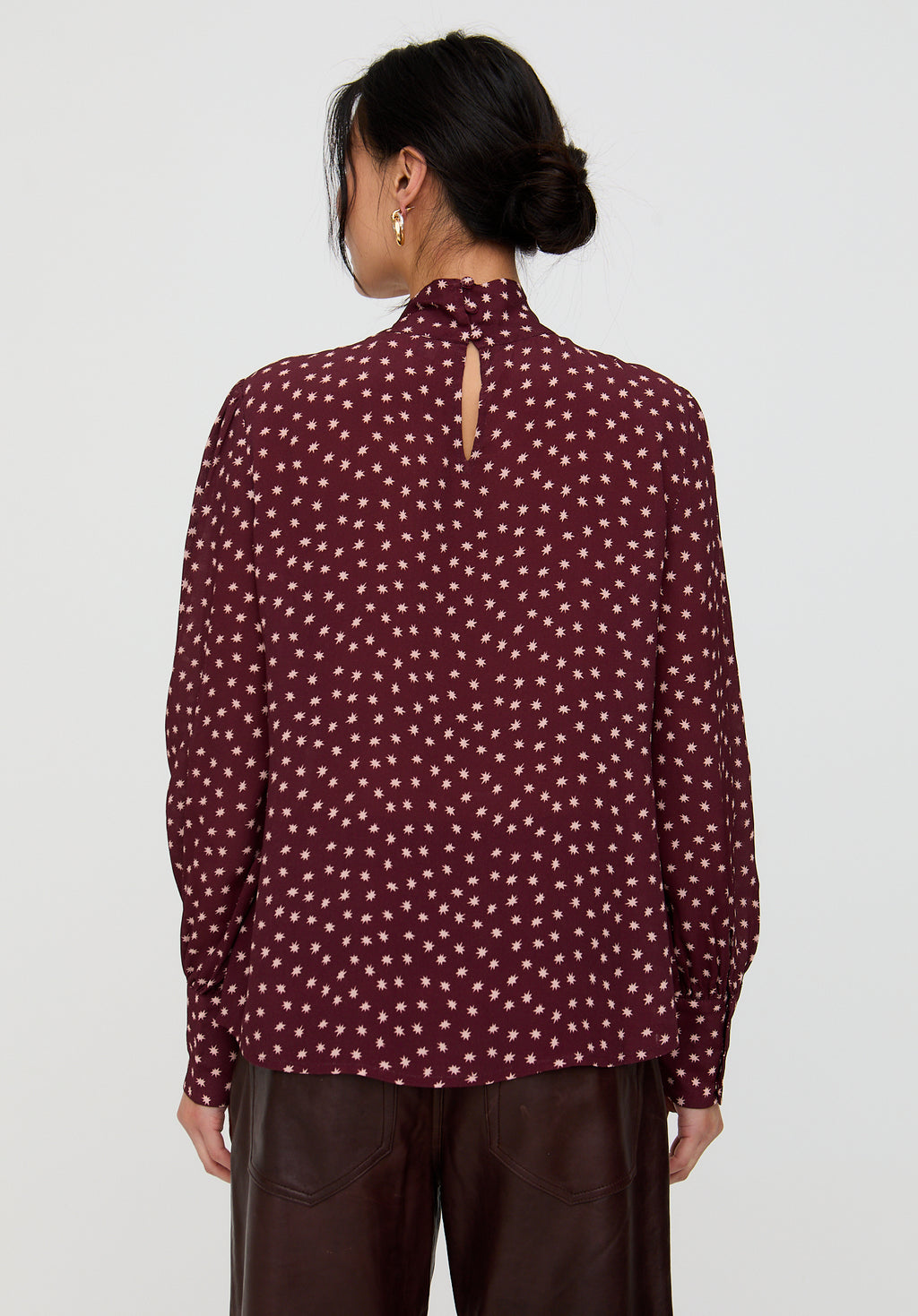 Person wearing a maroon blouse with white polka dots on a plain background
