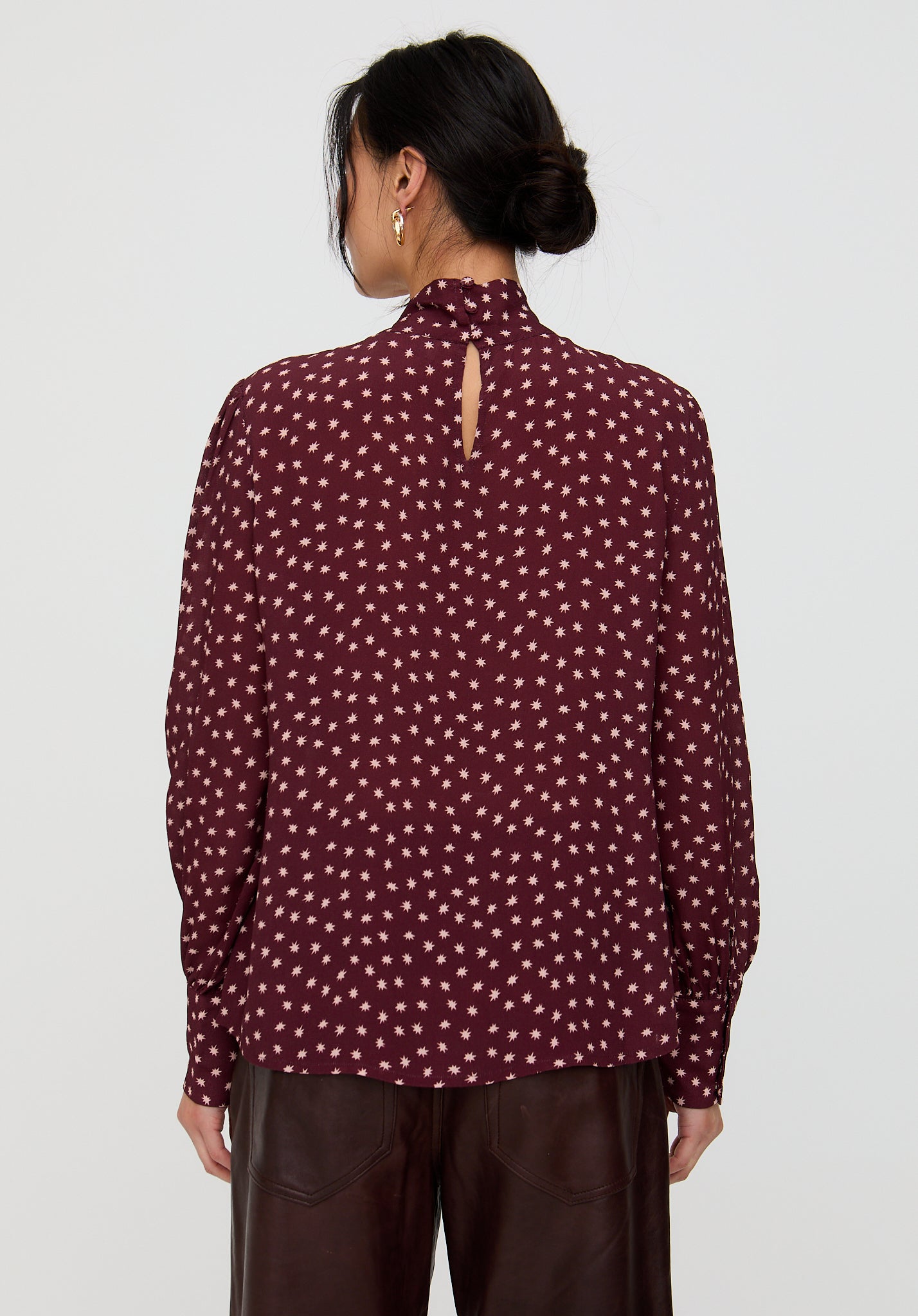 Person wearing a maroon blouse with white polka dots on a plain background