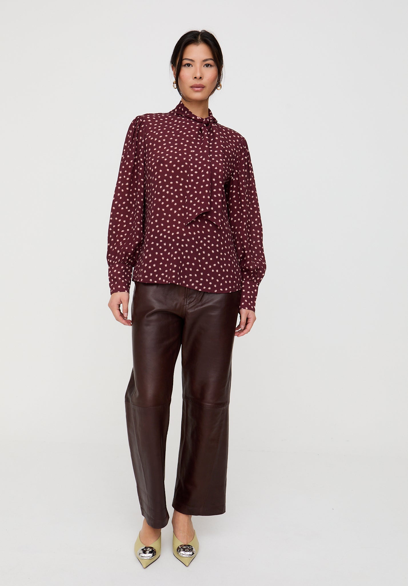 Woman wearing a patterned blouse and brown leather pants on a white background