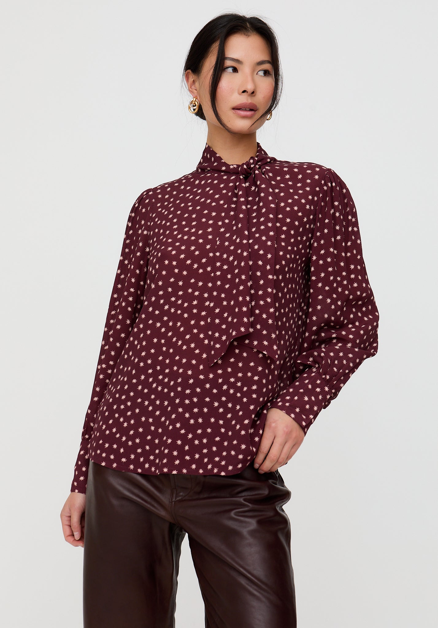 Woman wearing a patterned blouse and leather pants on a white background