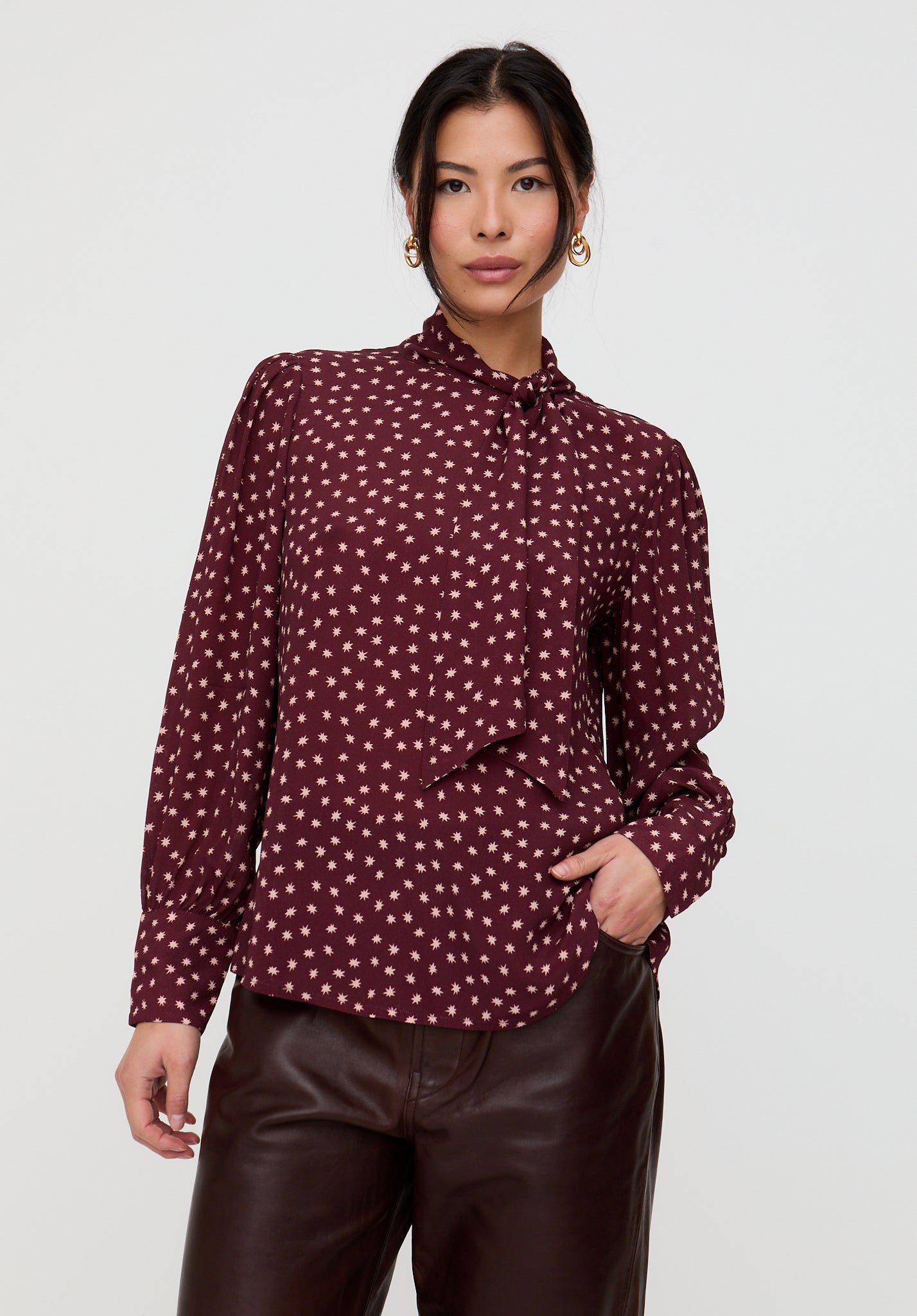 Woman wearing a burgundy blouse with white polka dots on a plain background