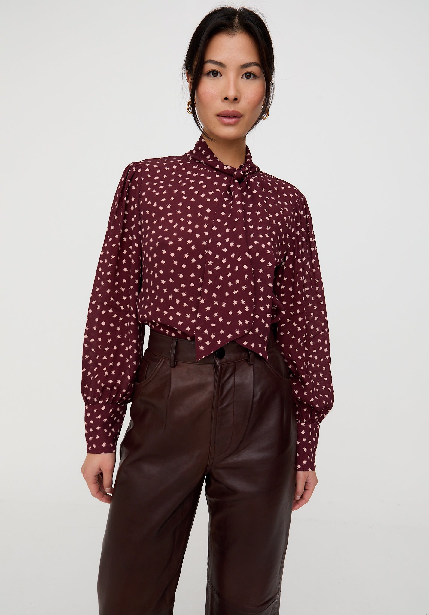 Woman wearing a patterned blouse and brown pants on a white background