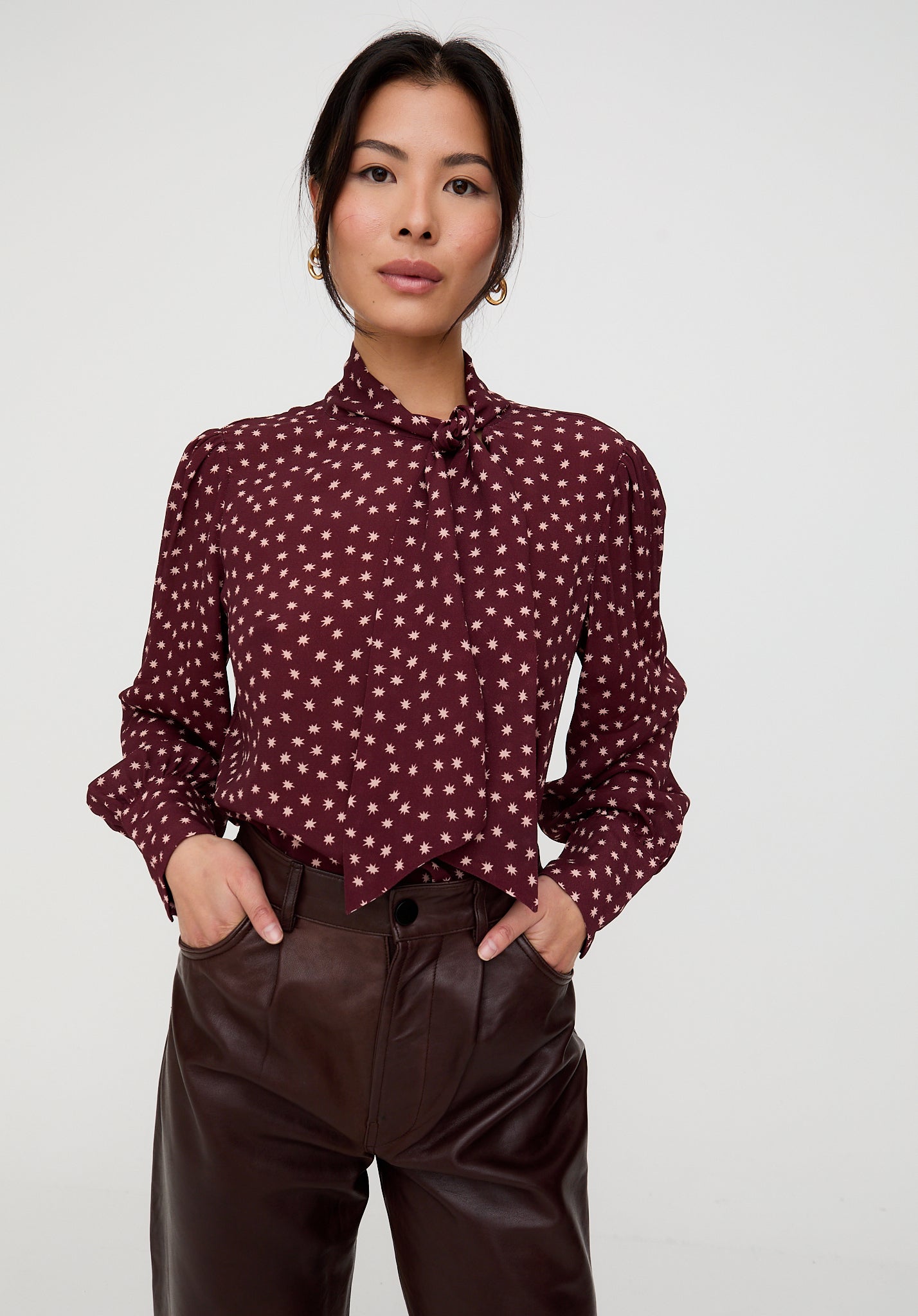 Woman wearing a burgundy blouse with white polka dots and brown pants on a white background