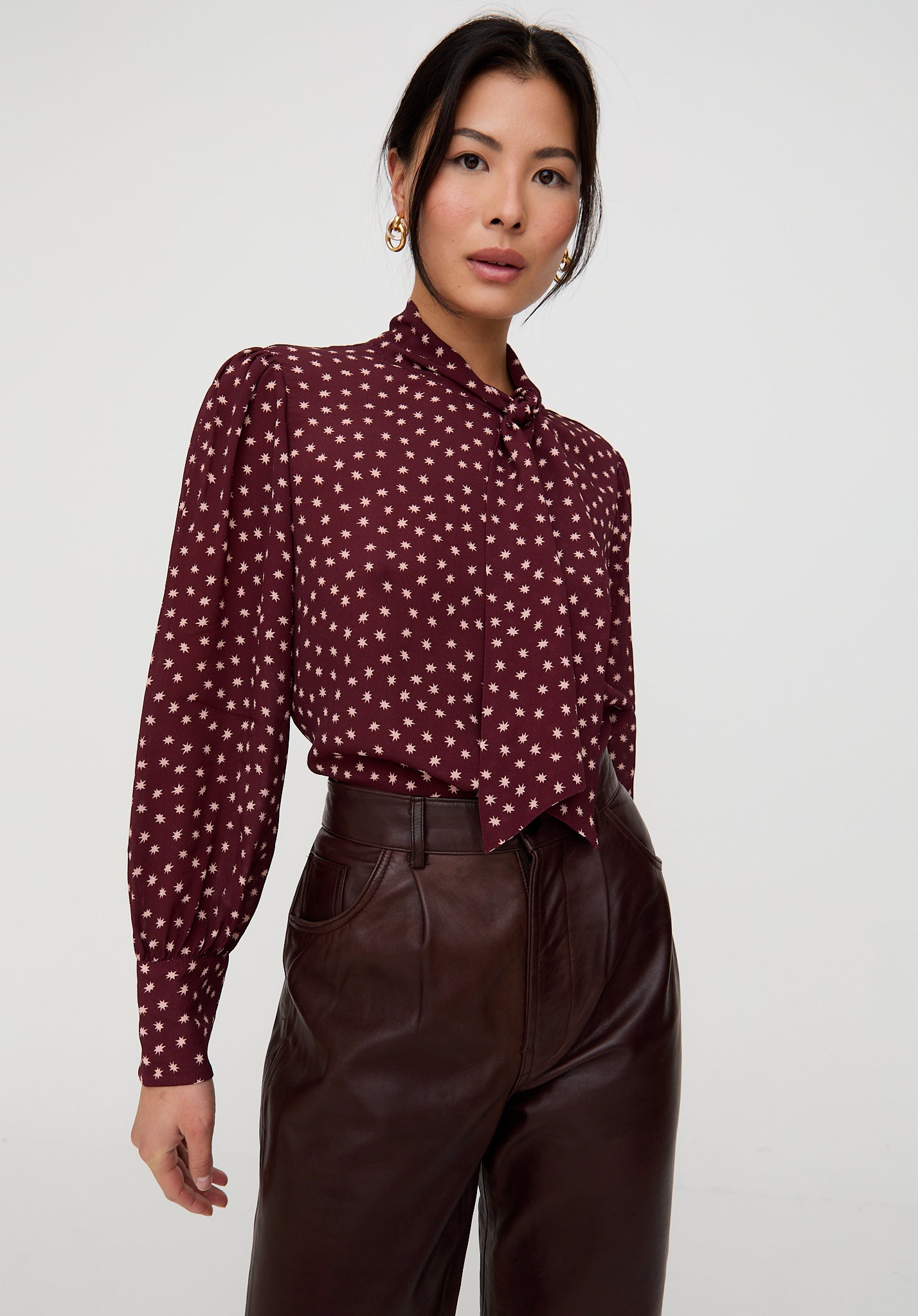 Woman wearing a burgundy blouse with white polka dots and brown pants on a white background