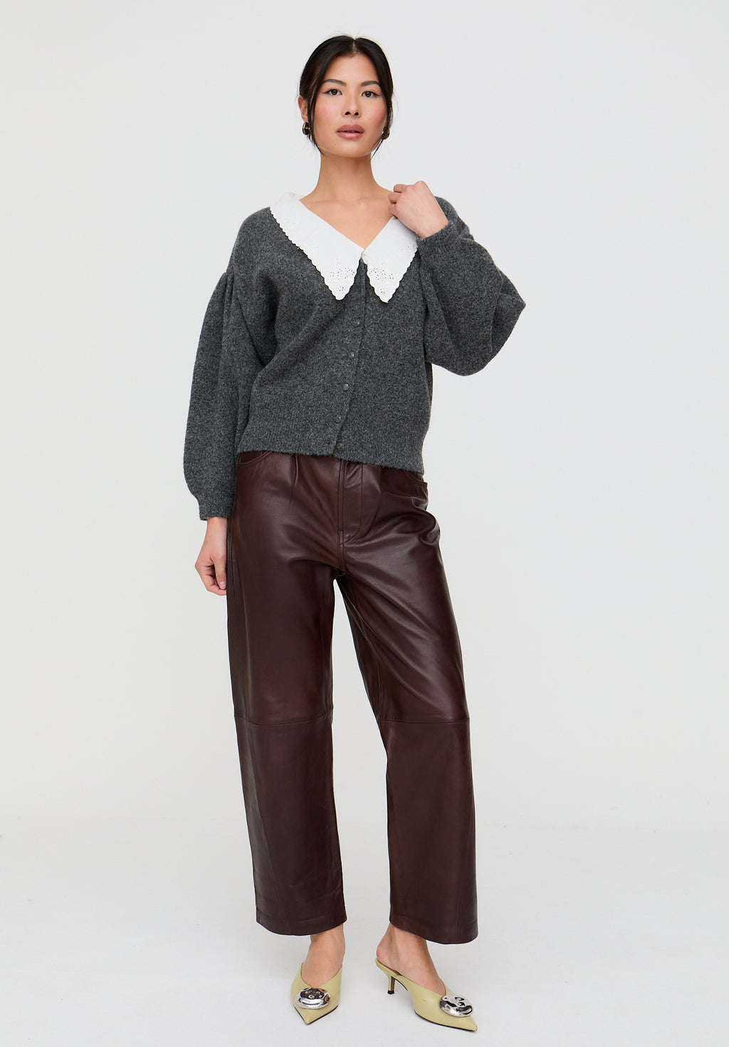 Woman wearing a gray cardigan with a white collar and brown leather pants on a white background