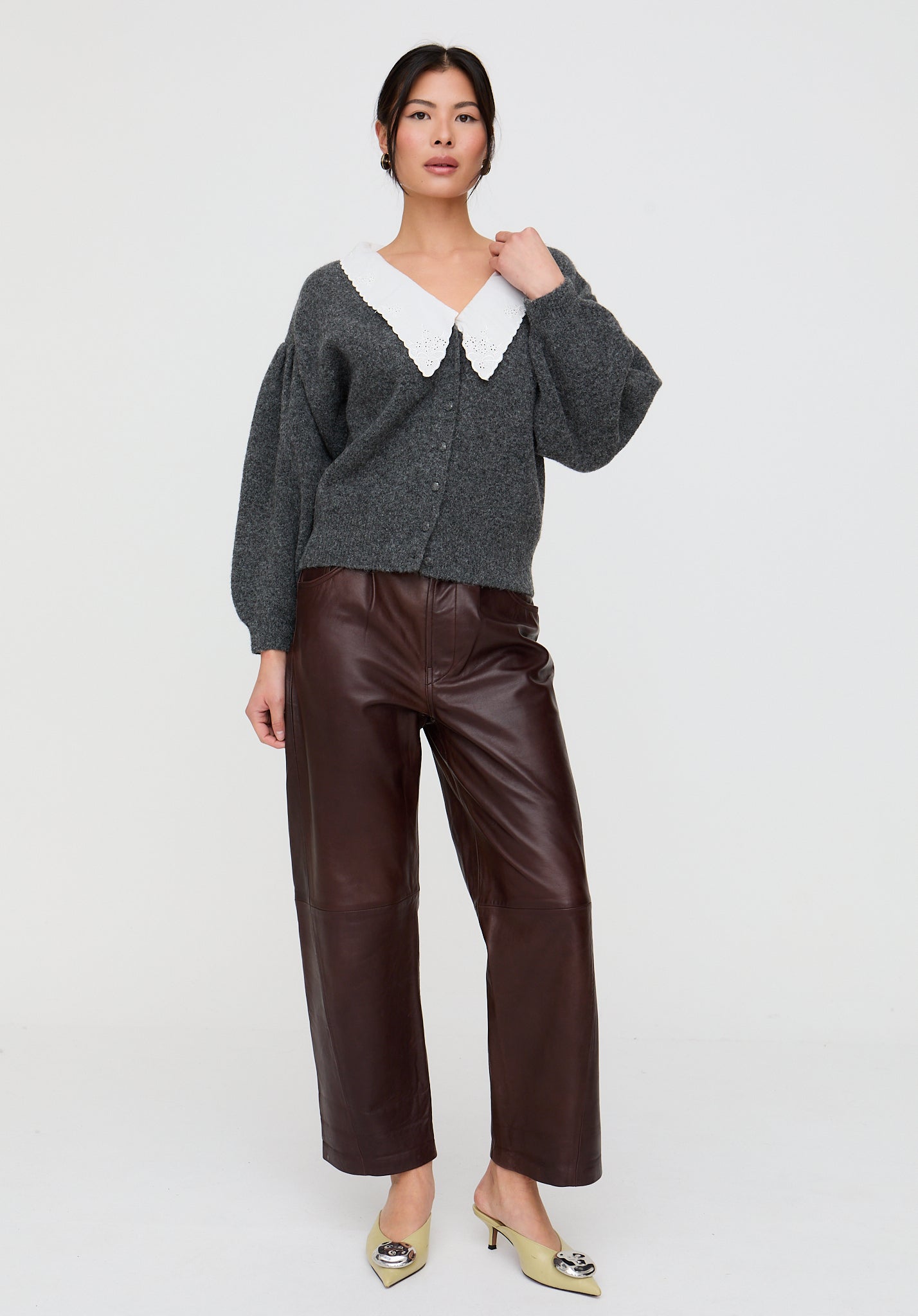 Woman wearing a gray cardigan with a white collar and brown leather pants on a white background