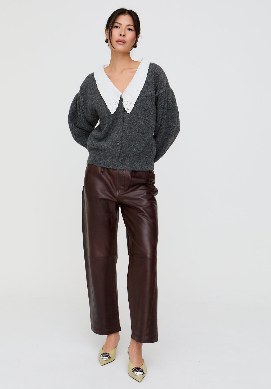 Woman wearing a gray cardigan with a white collar and brown pants on a white background