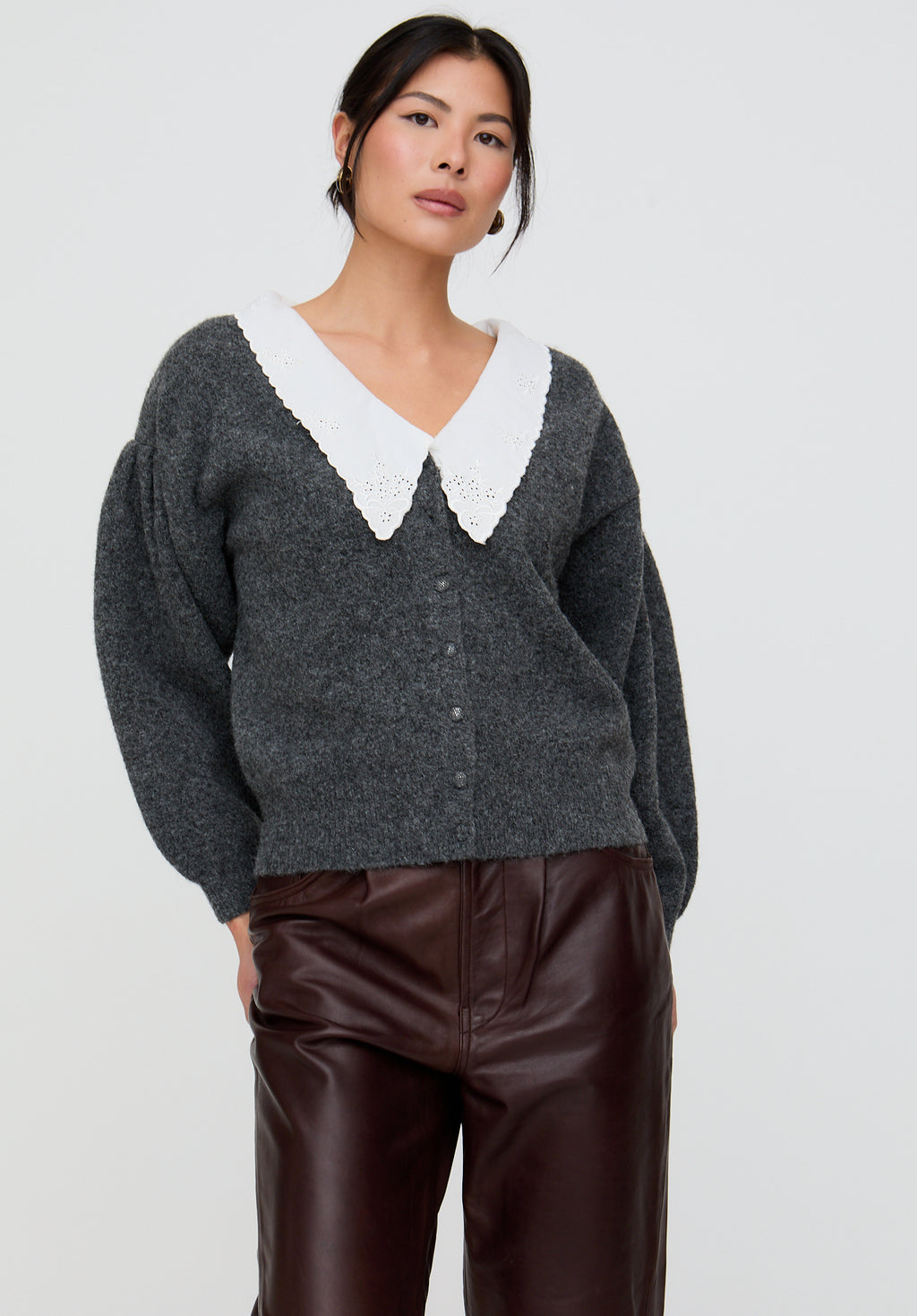 Woman wearing a dark gray sweater with a white collar against a plain background