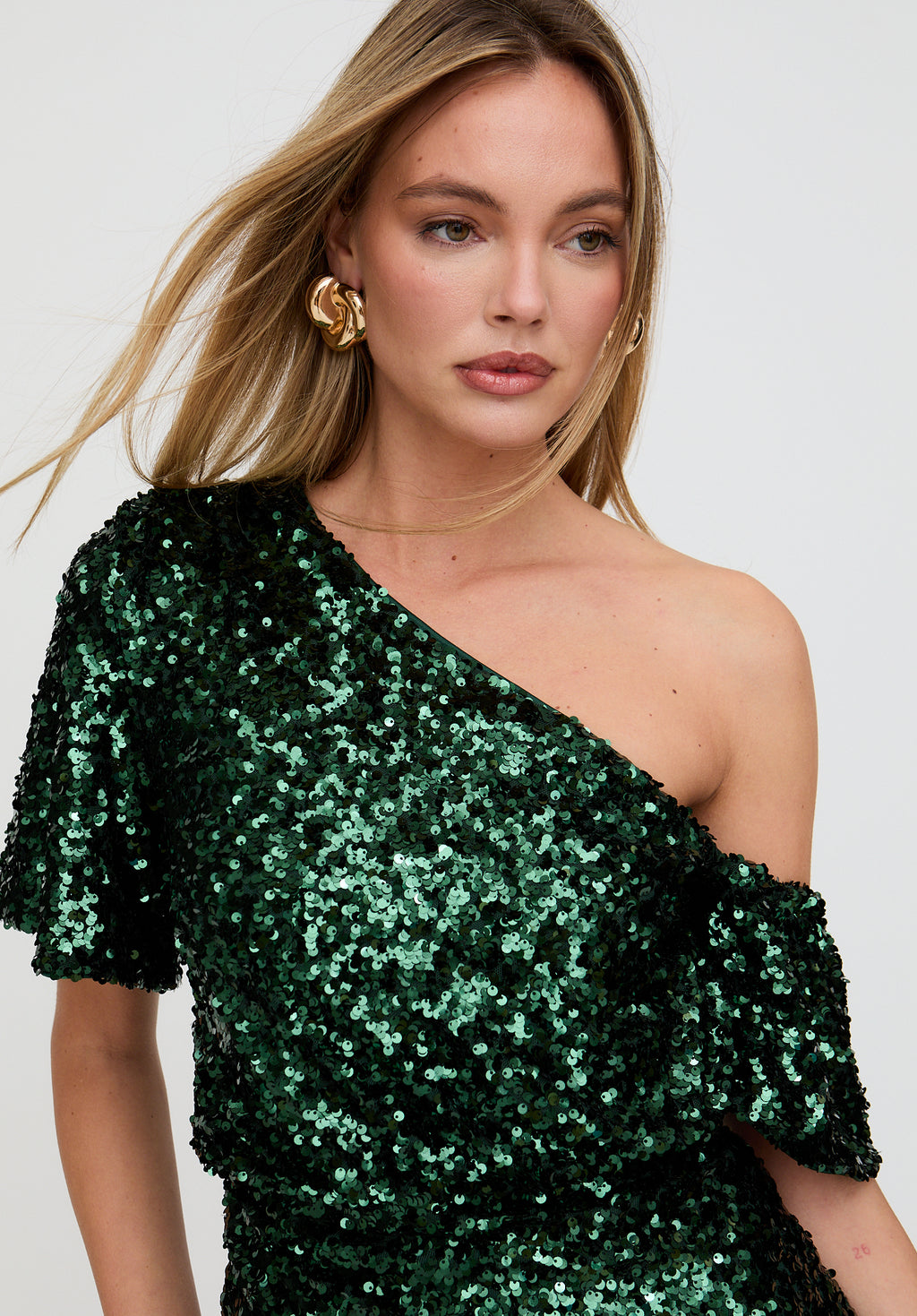 Woman wearing a green sequin one-shoulder dress against a white background