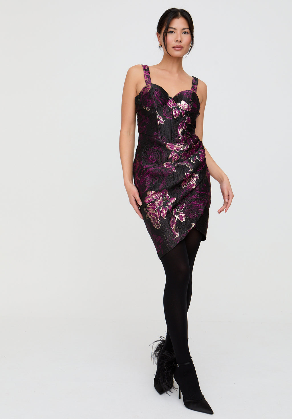 Woman wearing a floral dress with black tights and shoes on a white background