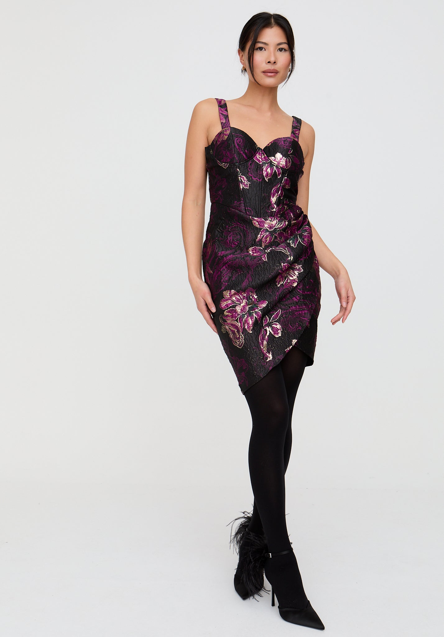 Woman wearing a floral dress with black tights and shoes on a white background