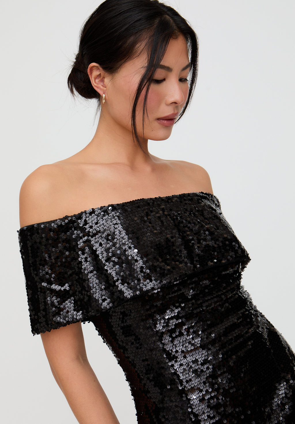 Woman wearing a black sequin off-shoulder dress against a plain background