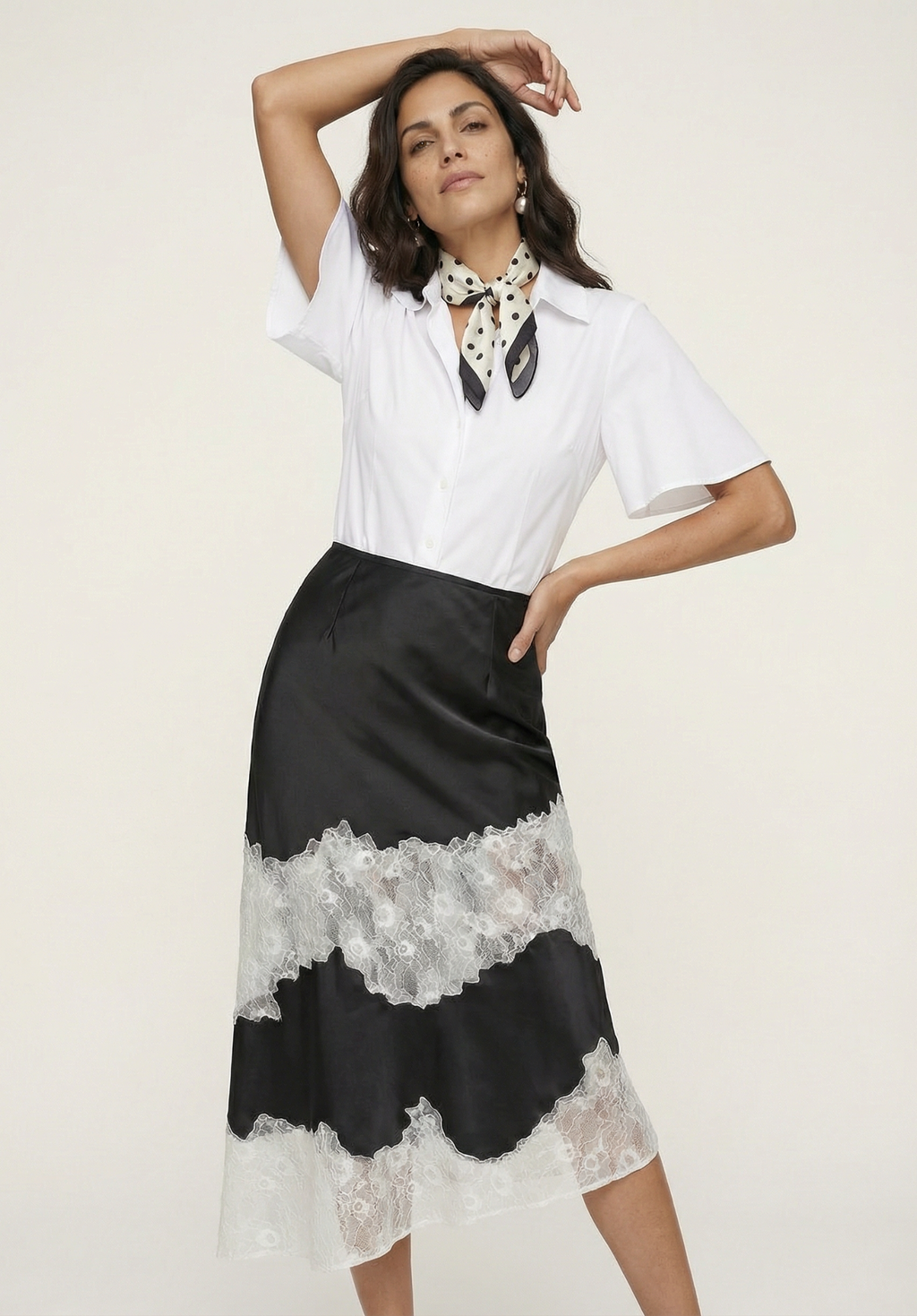 Woman wearing a white blouse and black skirt with lace details on a plain background