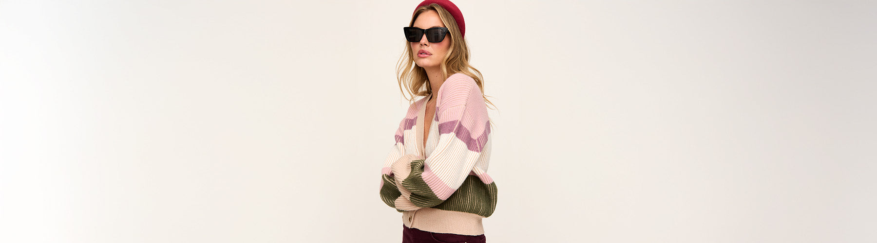 Woman wearing a colorful outfit with a pink top, green jacket, and sunglasses on a white background