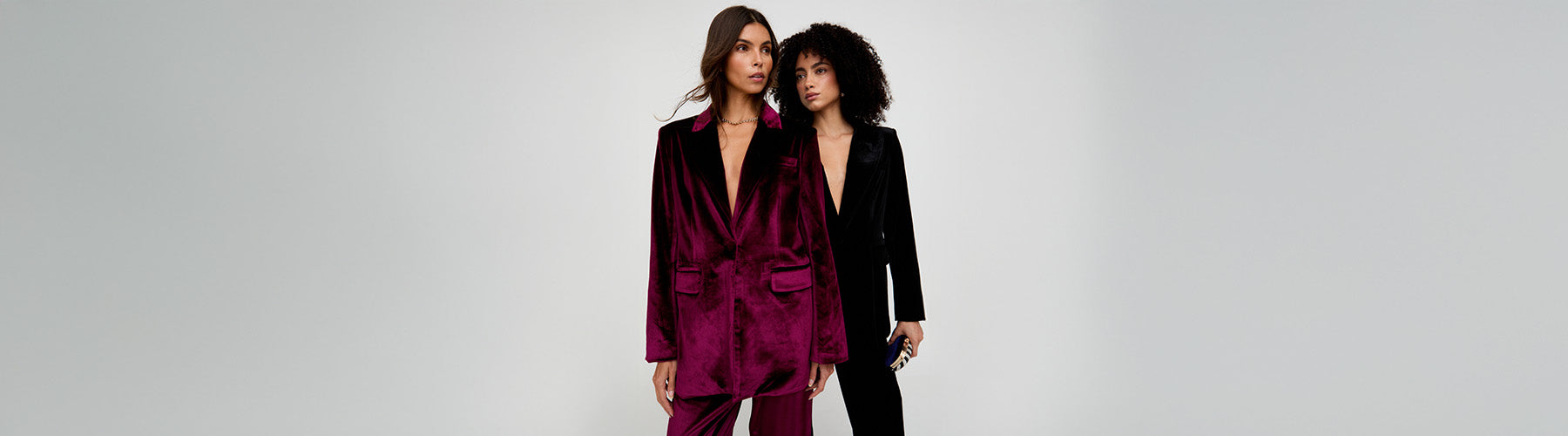 Two women wearing matching burgundy and black outfits against a gray background