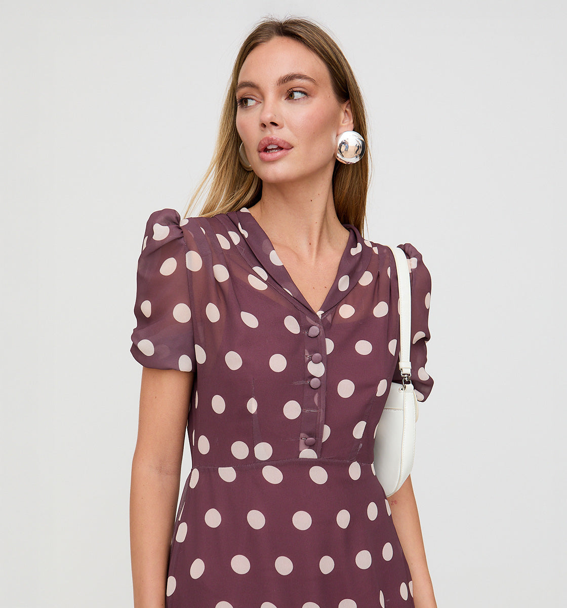 Woman wearing a purple dress with white polka dots on a plain background