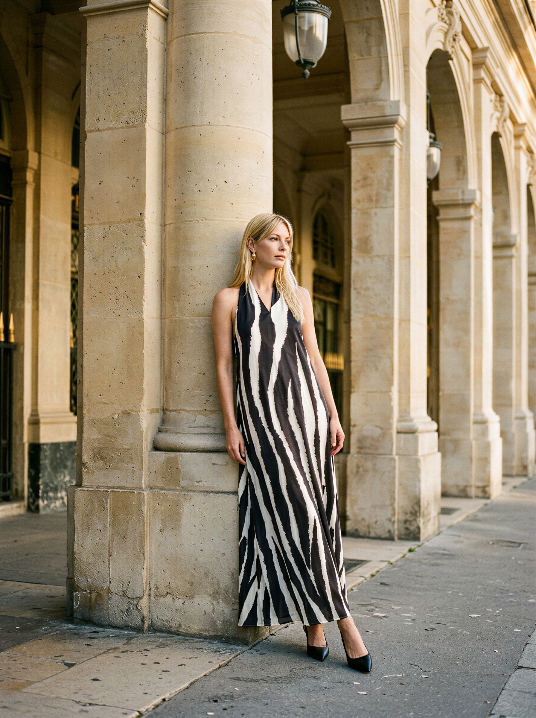 Woman in a black and white striped dress standing against a stone building with arches.